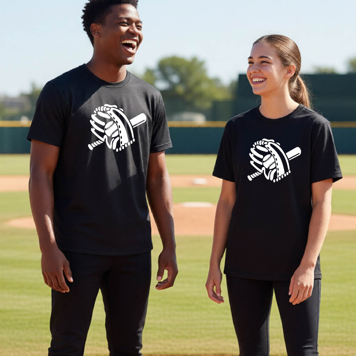 Two young athletes wearing matching shirts, smiling in front of a baseball diamond wearing black short-sleeve t-shirts with a white graphic of baseball mitt, bat and ball, printed on the front.