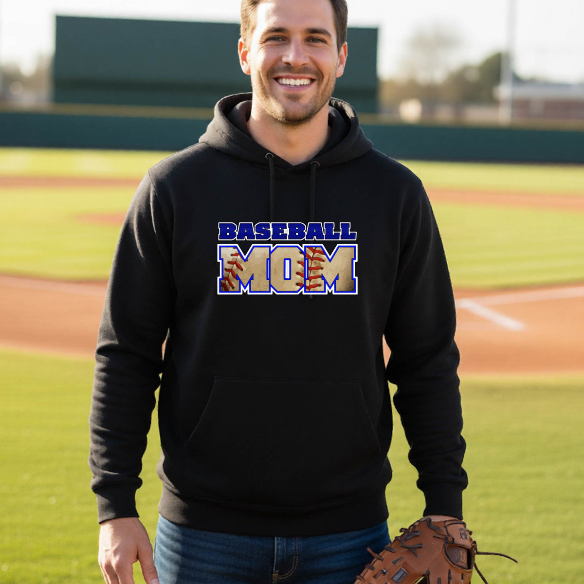 A man smiling in front of a baseball diamond wearing a black hoodie pullover with a colorful graphic of the words ‘BASEBALL MOM’ printed on the front.