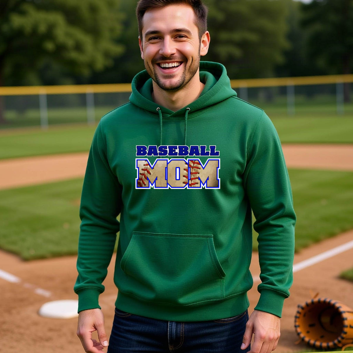 A man smiling in front of a baseball diamond wearing a green hoodie pullover with a colorful graphic of the words ‘BASEBALL MOM’ printed on the front.