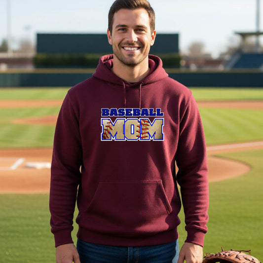 A man smiling in front of a baseball diamond wearing a maroon hoodie pullover with a colorful graphic of the words ‘BASEBALL MOM’ printed on the front.