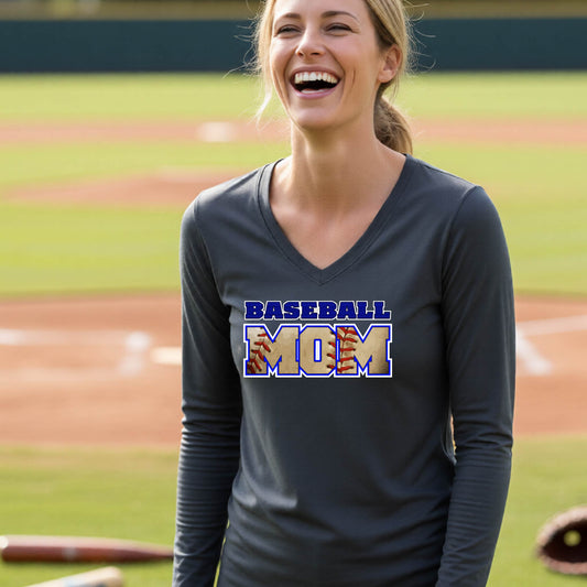 A woman smiling in front of a baseball diamond wearing a dark gray long-sleeve t-shirt with a colorful graphic of the words ‘BASEBALL MOM’ printed on the front.