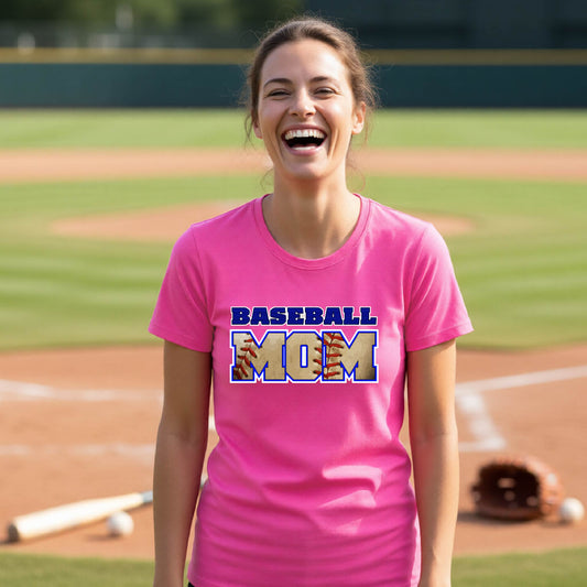 A woman smiling in front of a baseball diamond wearing a pink long-sleeve t-shirt with a colorful graphic of the words ‘BASEBALL MOM’ printed on the front.