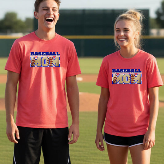 Two youth athletes wearing matching shirts, smiling in front of a baseball diamond wearing coral colored short-sleeve t-shirt with a colorful graphic of the words ‘BASEBALL MOM’ printed on the front.