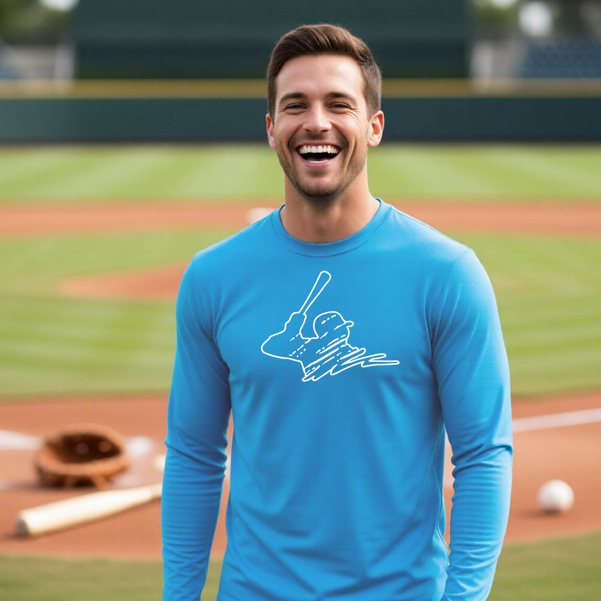 A man smiling in front of a baseball diamond wearing a bright blue long-sleeve t-shirt, with a white graphic of an outline of a baseball player up to bat, printed on the front.
