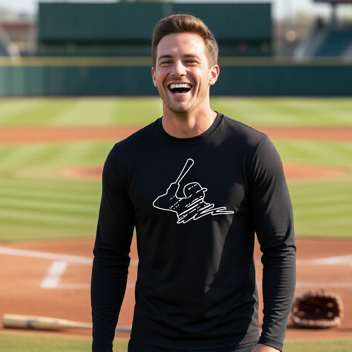 A man smiling in front of a baseball diamond wearing a black long-sleeve t-shirt, with a white graphic of an outline of a baseball player up to bat, printed on the front.