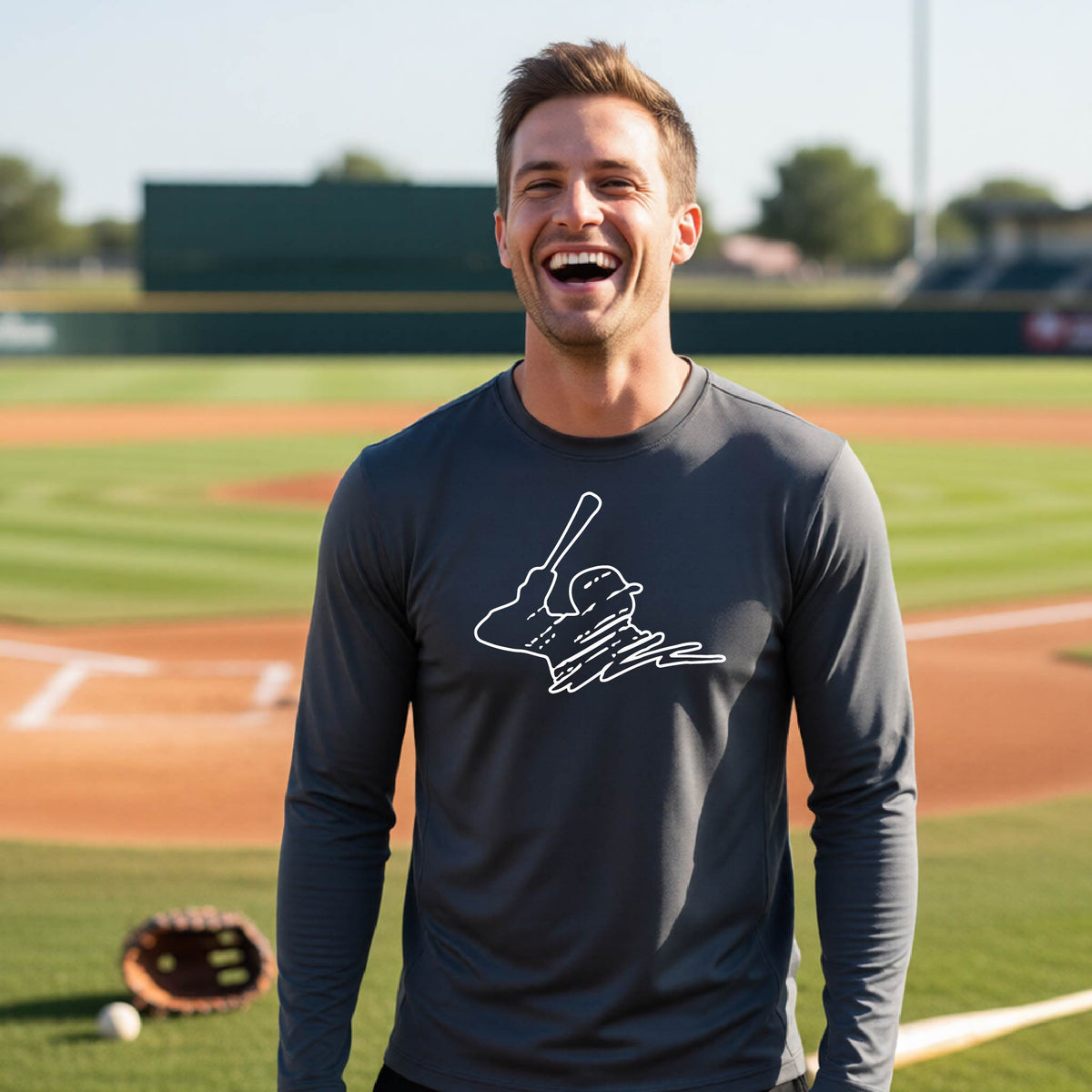 A man smiling in front of a baseball diamond wearing a dark gray long-sleeve t-shirt, with a white graphic of an outline of a baseball player up to bat, printed on the front.