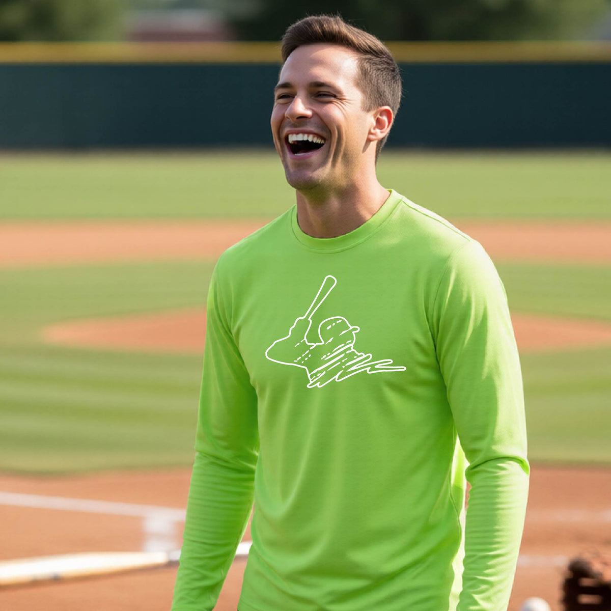 A man smiling in front of a baseball diamond wearing a lime green long-sleeve t-shirt, with a white graphic of an outline of a baseball player up to bat, printed on the front.