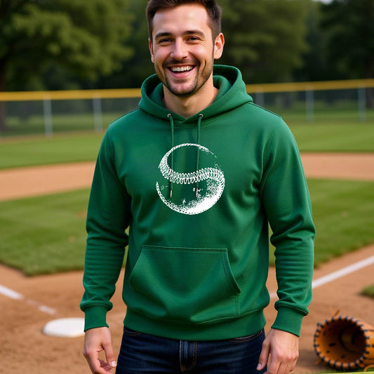 A man smiling in front of a baseball diamond wearing a green hoodie pullover, with a white artistic graphic of a baseball, printed on the front.