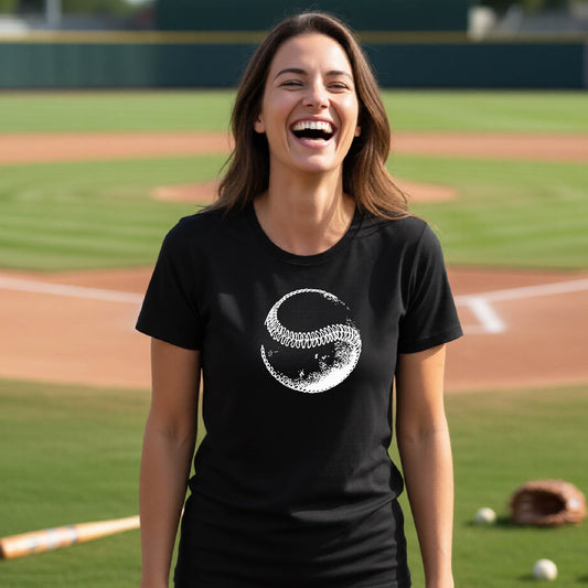 A woman smiling in front of a baseball diamond wearing a black short-sleeve t-shirt, with a white artistic graphic of a baseball printed on the front.