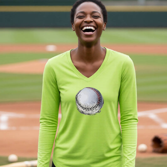 A woman smiling in front of a baseball diamond wearing a lime green long-sleeve t-shirt, with a white and red graphic of an outline of a sketched retro baseball, printed on the front.
