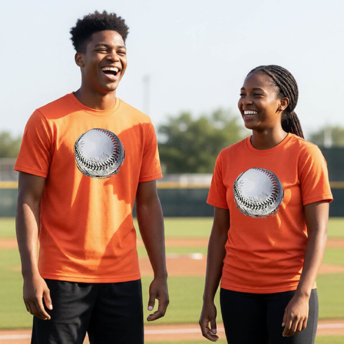Two youth athletes wearing matching shirts, smiling in front of a baseball diamond wearing orange  long-sleeve t-shirts with a white and red graphic of a sketched retro baseball, printed on the front.