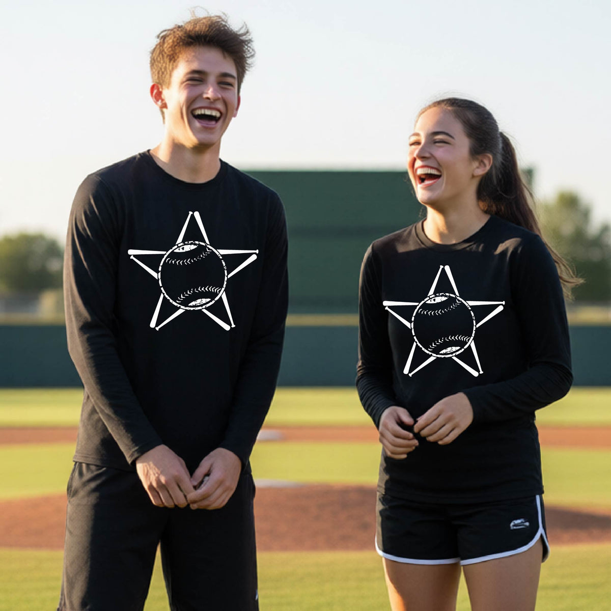 A man smiling in front of a baseball diamond wearing a black long-sleeve t-shirt, with a white graphic of a star made of baseball bats and a ball in the middle, printed on the front.