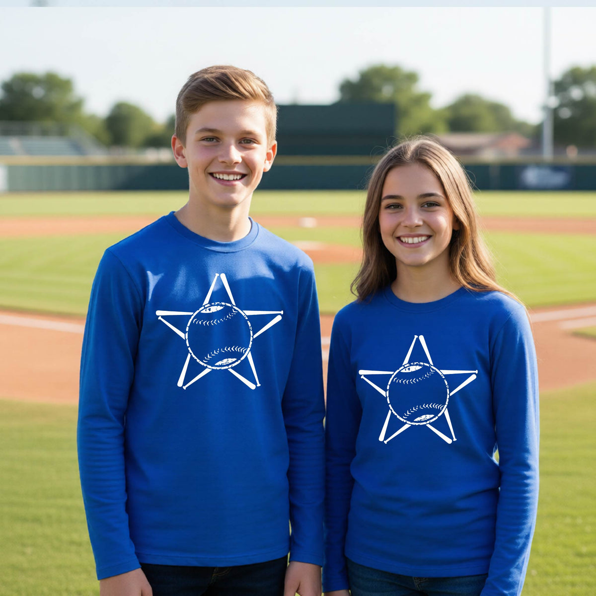 A man smiling in front of a baseball diamond wearing a royal blue long-sleeve t-shirt, with a white graphic of a star made of baseball bats and a ball in the middle, printed on the front.