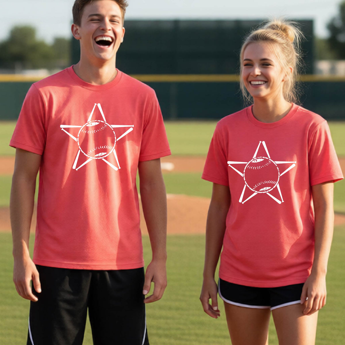 Two youth athletes wearing matching shirts, smiling in front of a baseball diamond wearing coral pink  long-sleeve t-shirts with a white graphic of a star made of baseball bats and a ball in the middle, printed on the front.