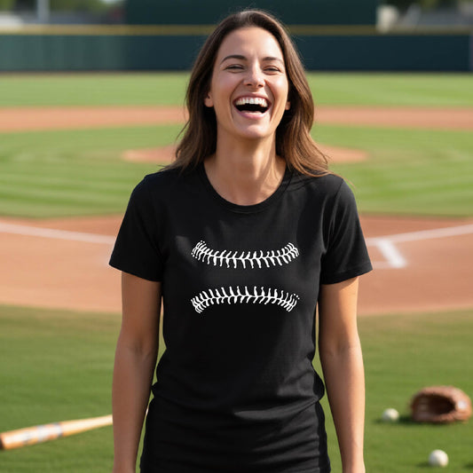 A woman smiling in front of a baseball diamond wearing a black short-sleeve t-shirt, with a white graphic of baseball stitches, printed on the front.