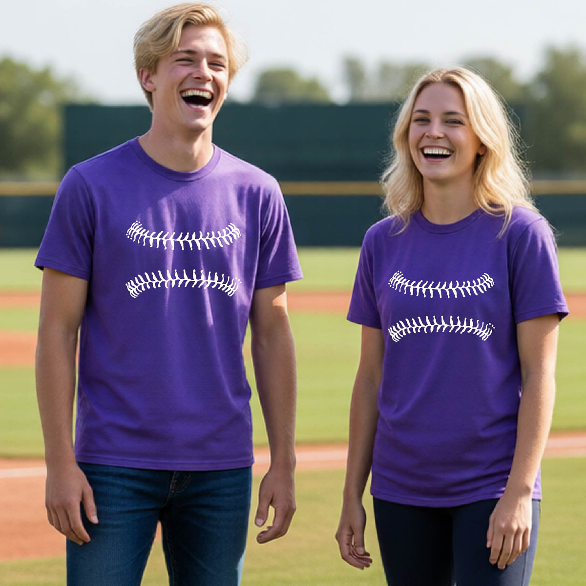 Two youth athletes wearing matching shirts, smiling in front of a baseball diamond wearing purple short-sleeve t-shirts with a white graphic of baseball stitches, printed on the front.