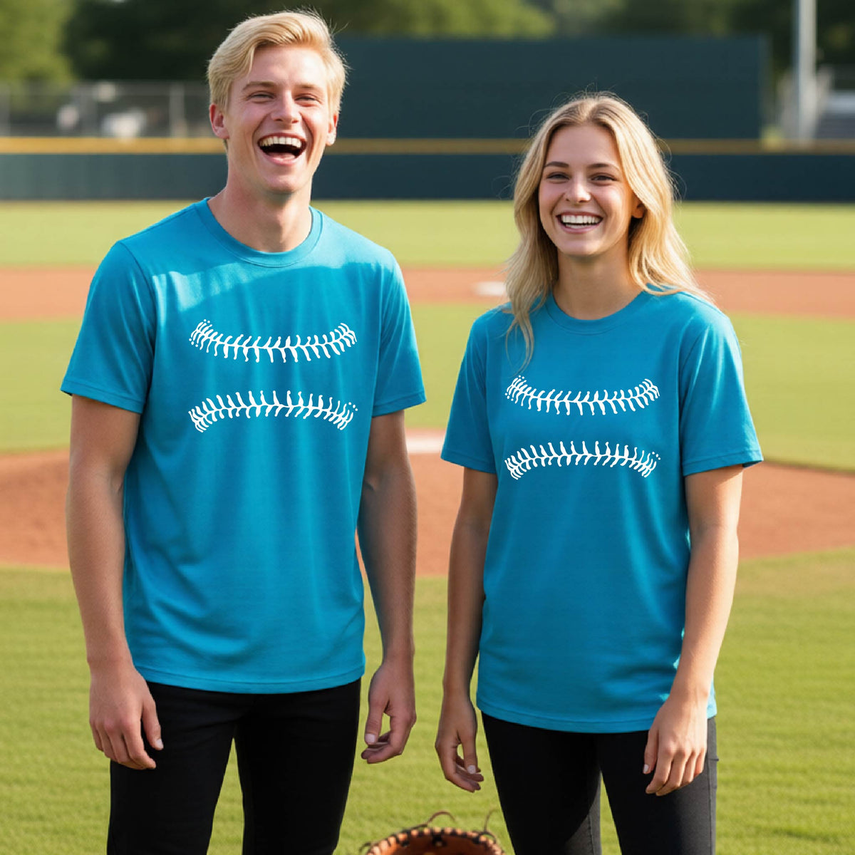 Two youth athletes wearing matching shirts, smiling in front of a baseball diamond wearing bright blue short-sleeve t-shirts with a white graphic of baseball stitches, printed on the front.