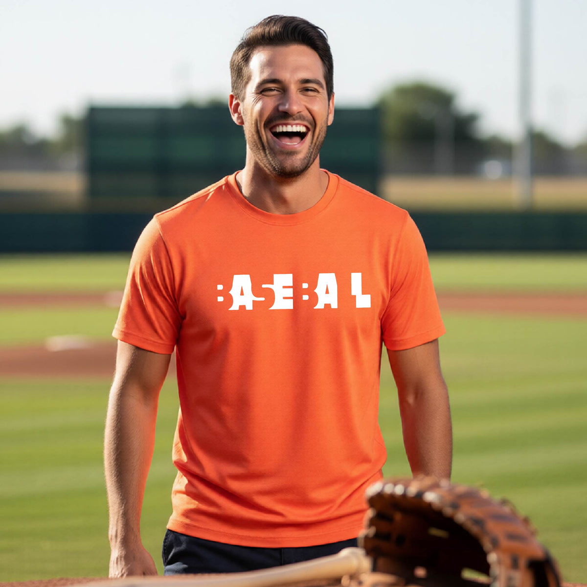 A man laughing on a baseball field wearing an orange t-shirt with the white text 'BASEBALL' printed on the front. A baseball bat, glove, and ball are visible in the foreground.