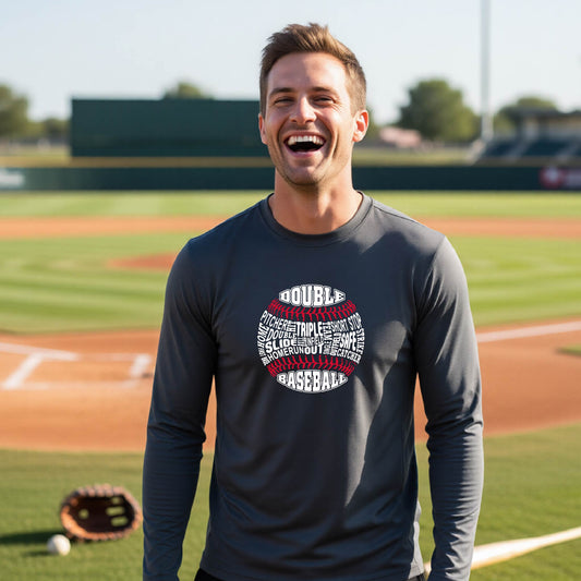 A man smiling in front of a baseball diamond wearing a dark gray long-sleeve t-shirt, with a white and red graphic of a baseball made up of baseball words, printed on the front of the shirt.