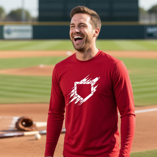 A man smiling in front of a baseball diamond wearing a red  long-sleeve t-shirt, with an artistic white graphic of a sketch of baseball home plate, printed on the front of the shirt.