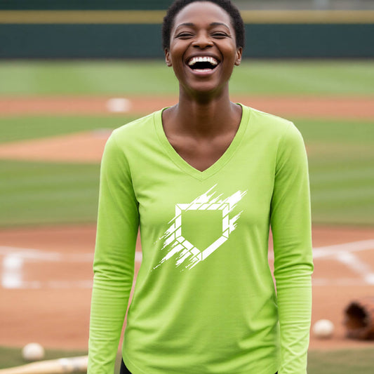 A woman smiling in front of a baseball diamond wearing a lime green long-sleeve t-shirt, with an artistic white graphic of a sketch of baseball home plate, printed on the front of the shirt.