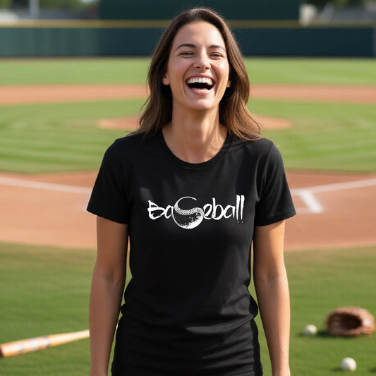 A woman smiling in front of a baseball diamond wearing a black short-sleeve t-shirt, with an artistic white graphic of a sketch of the word BASEBALL” in a curved font with the S replaced by a baseball, printed on the front of the shirt.