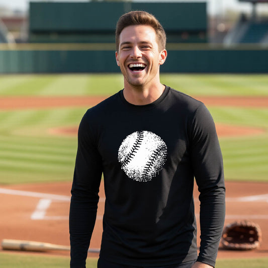 A man smiling in front of a baseball diamond wearing a black long-sleeve t-shirt, with an artistic white graphic of a retro looking baseball, printed on the front of the shirt.