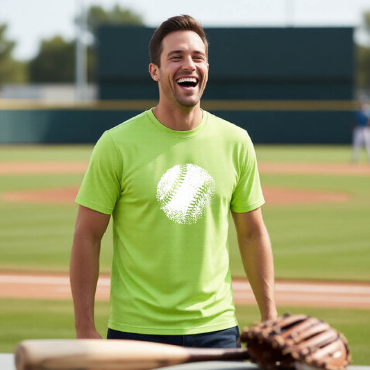 A man smiling in front of a baseball diamond wearing a lime green short-sleeve t-shirt, with an artistic white graphic of a retro looking baseball, printed on the front of the shirt.