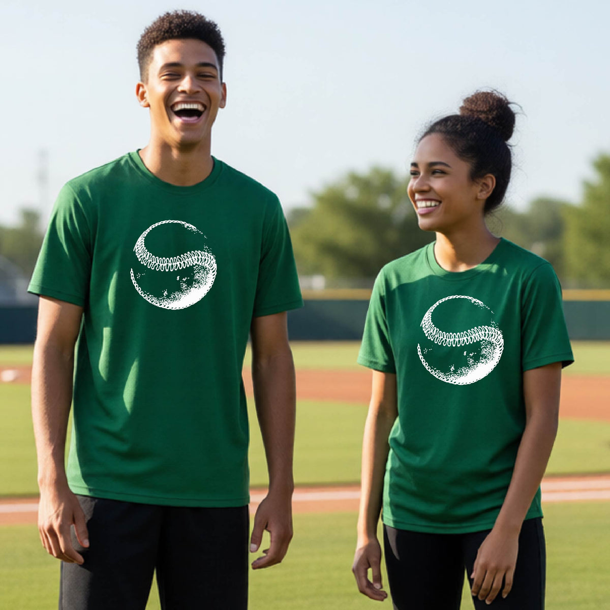 Two youth athletes wearing matching shirts, smiling in front of a baseball diamond wearing green short-sleeve t-shirts, with a white artistic graphic of a baseball, printed on the front.