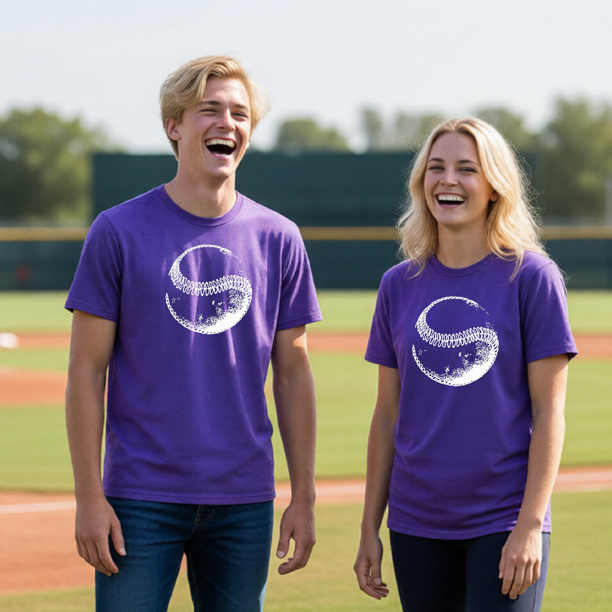 Two youth athletes wearing matching shirts, smiling in front of a baseball diamond wearing purple short-sleeve t-shirts, with a white artistic graphic of a baseball, printed on the front.
