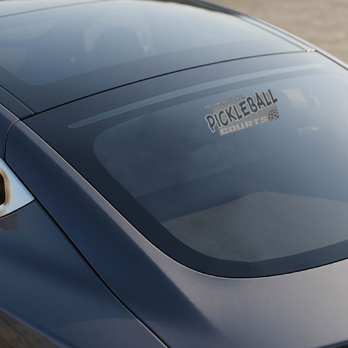 A car window showing a 'FOLLOW ME TO THE PICKLEBALL COURTS' vinyl decal sticker applied to a vehicle window. 