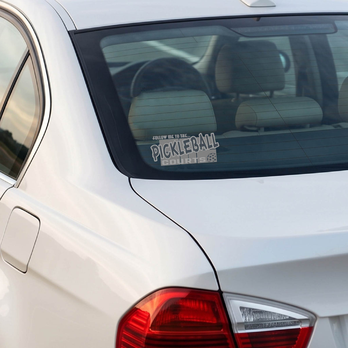 A car window showing a 'FOLLOW ME TO THE PICKLEBALL COURTS' vinyl decal sticker applied to a vehicle window. 