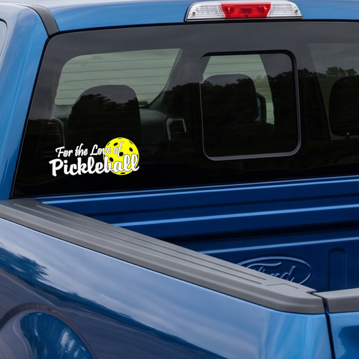 A close-up of a car decal and a pickleball graphic of ‘FOR THE LOVE OF PICKLEBALL’ in white with a yellow pickleball behind it graphic on the front.