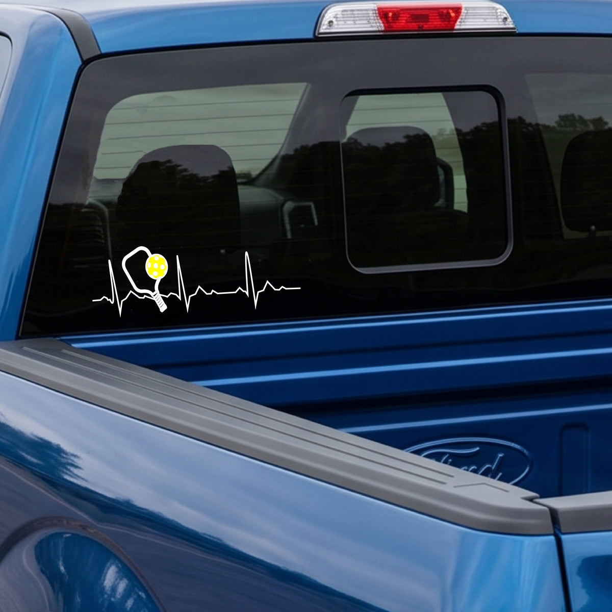 A close-up of a car decal showing a white pickleball graphic of a heartbeat EKG including a pickleball paddle and a yellow pickleball. 