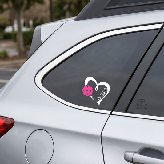A close-up of a car decal with a white heart and a pink pickleball graphic with the tExt inside the heart 'PICKLEBALL"