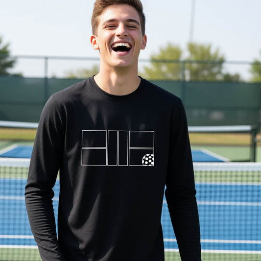 A young person laughing on a pickleball court, wearing a black long-sleeve t-shirt with a white geometric graphic on the front of pickleball court and pickleball.