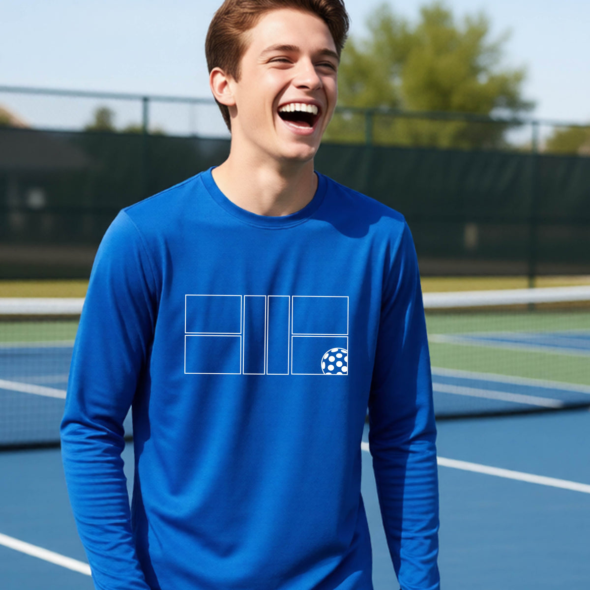 A young person laughing on a pickleball court, wearing a royal blue long-sleeve t-shirt with a white geometric graphic on the front of pickleball court and pickleball.
