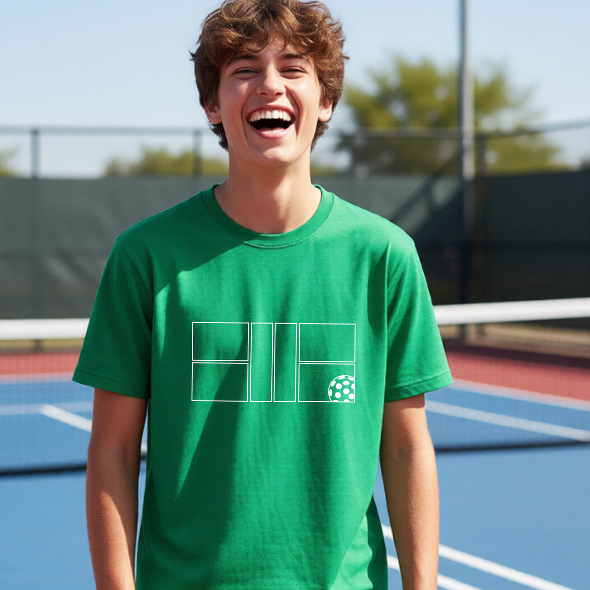 A young person laughing on a pickleball court, wearing a green short-sleeve t-shirt with a white geometric graphic on the front of pickleball court and pickleball.