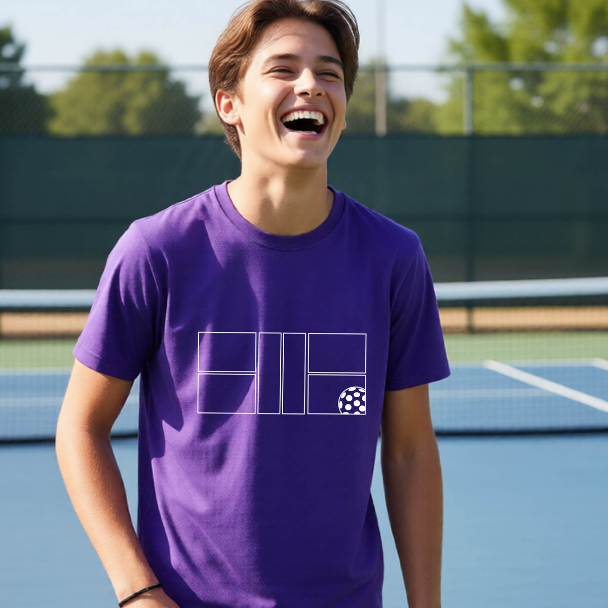 A young person laughing on a pickleball court, wearing a purple short-sleeve t-shirt with a white geometric graphic on the front of pickleball court and pickleball.