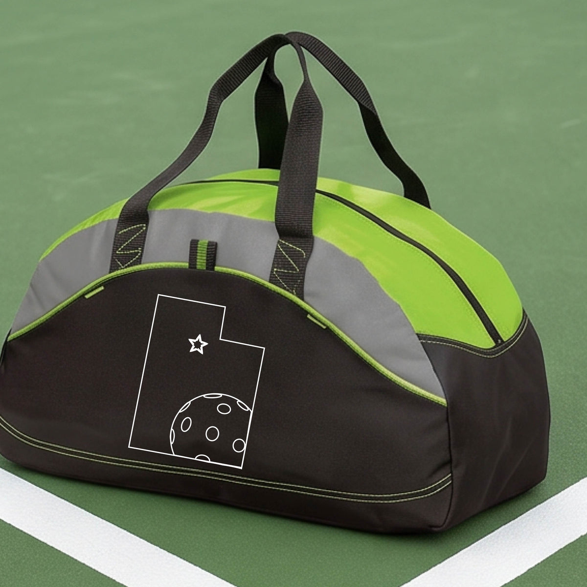 A close-up of a medium-size lime green, black with gray panels duffel bag, with a white graphic of the State of Utah , including an outline of a white pickleball in the lower right corner and a star outline in the center of the graphic, on the front of the bag