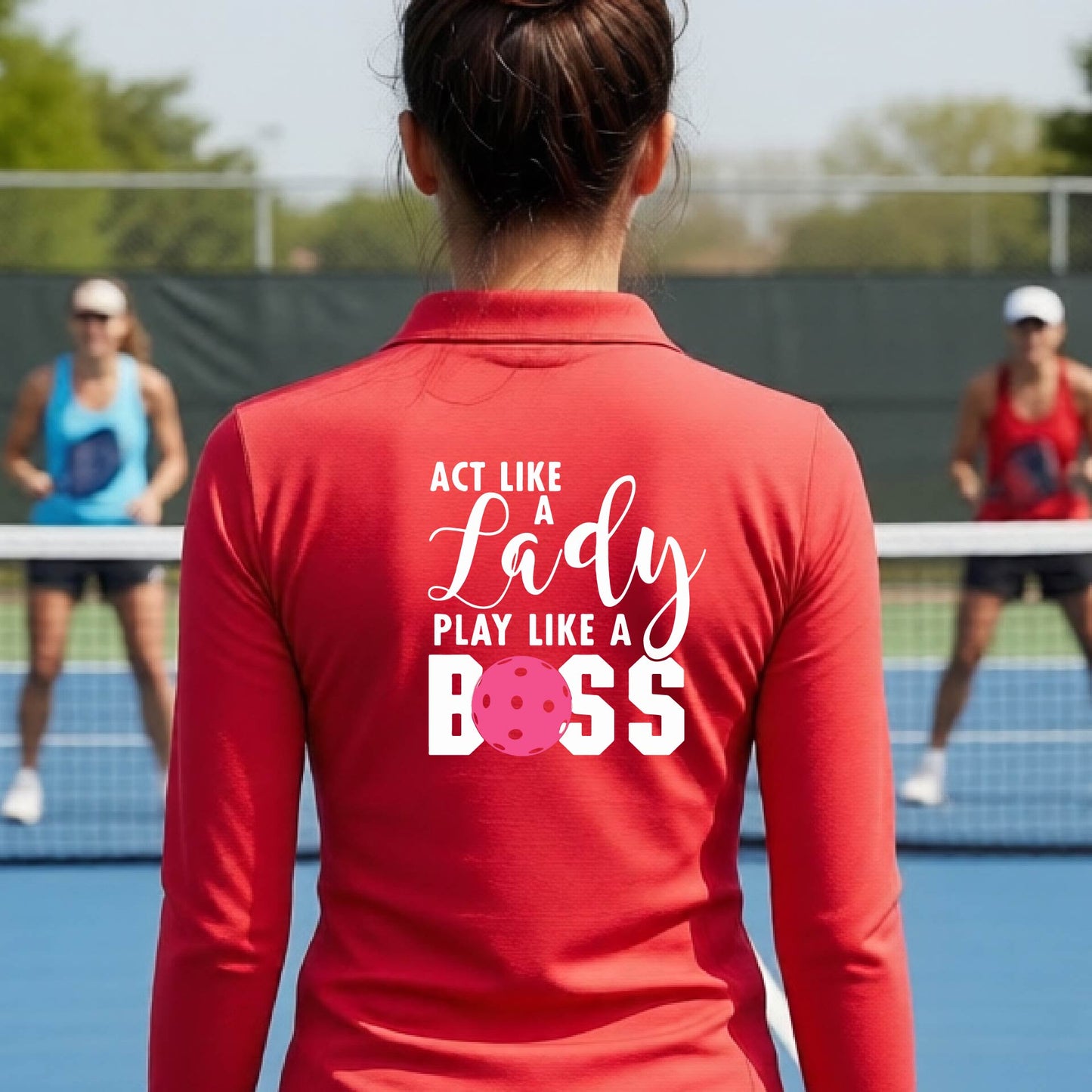A woman wearing a red quarter-zip long-sleeve athletic shirt on a pickleball court. The back of the shirt features the text 'ACT LIKE A Lady PLAY LIKE A BOSS' in white, with a pink pickleball graphic replacing the letter 'O' in 'BOSS'.