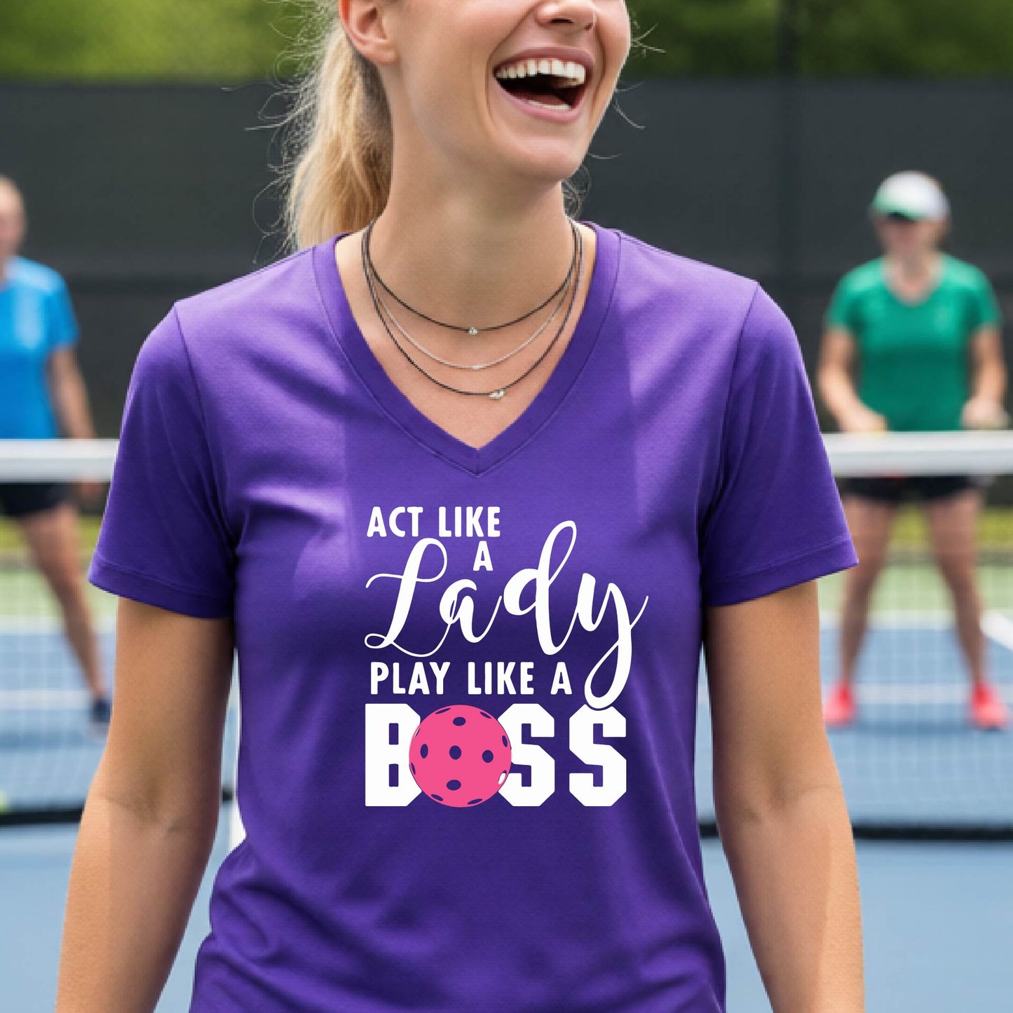 A woman wearing a purple V-neck t-shirt with a graphic print that reads 'ACT LIKE A Lady PLAY LIKE A BOSS' in white, featuring a pink pickleall ball graphic for the letter 'O'. 