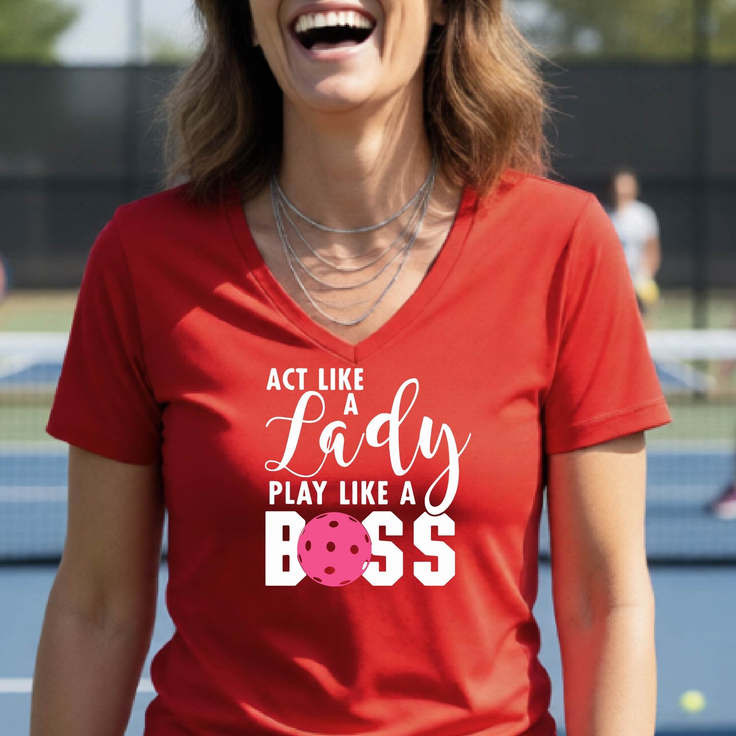 A woman wearing a red V-neck t-shirt with a graphic print that reads 'ACT LIKE A Lady PLAY LIKE A BOSS' in white, featuring a pink pickleall ball graphic for the letter 'O'. 