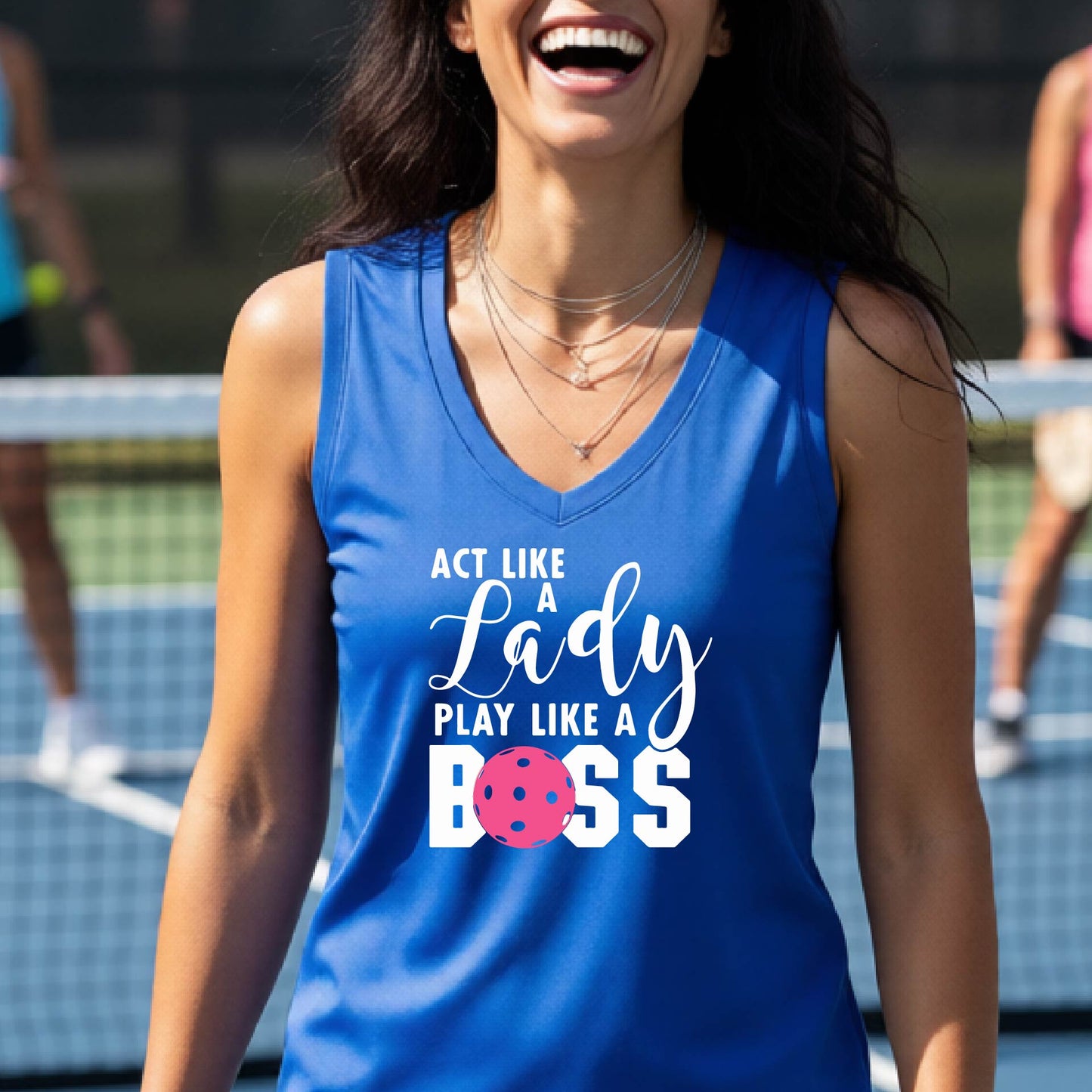 A woman on a pickkleball court wearing a royal blue sleeveless tank top with a white and pink graphic that reads 'ACT LIKE A Lady PLAY LIKE A BOSS'.