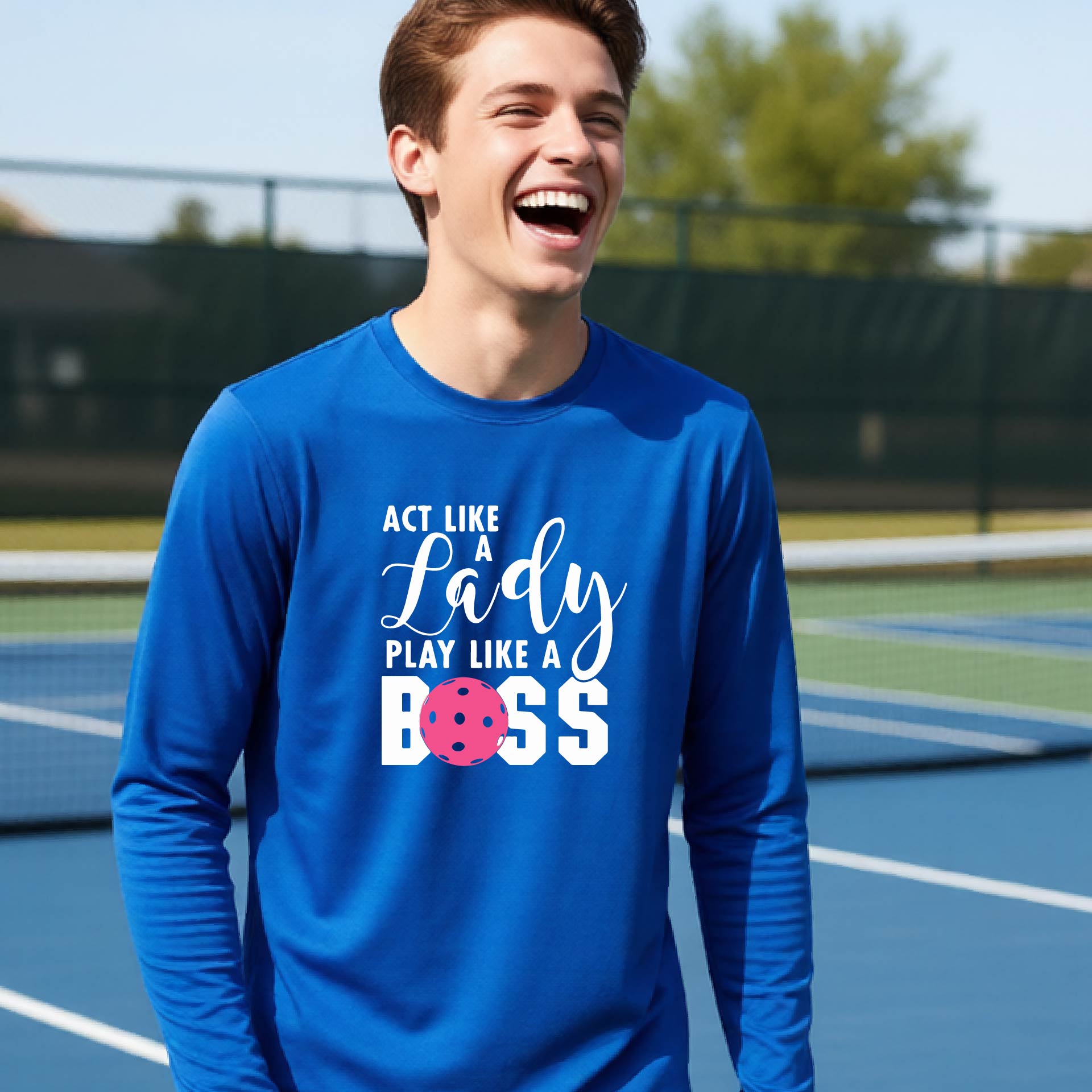 A young person laughing on a pickleball court wearing a royal blue long-sleeve t-shirt with the text 'ACT LIKE A Lady PLAY LIKE A BOSS' and a pink polka-dot graphic.