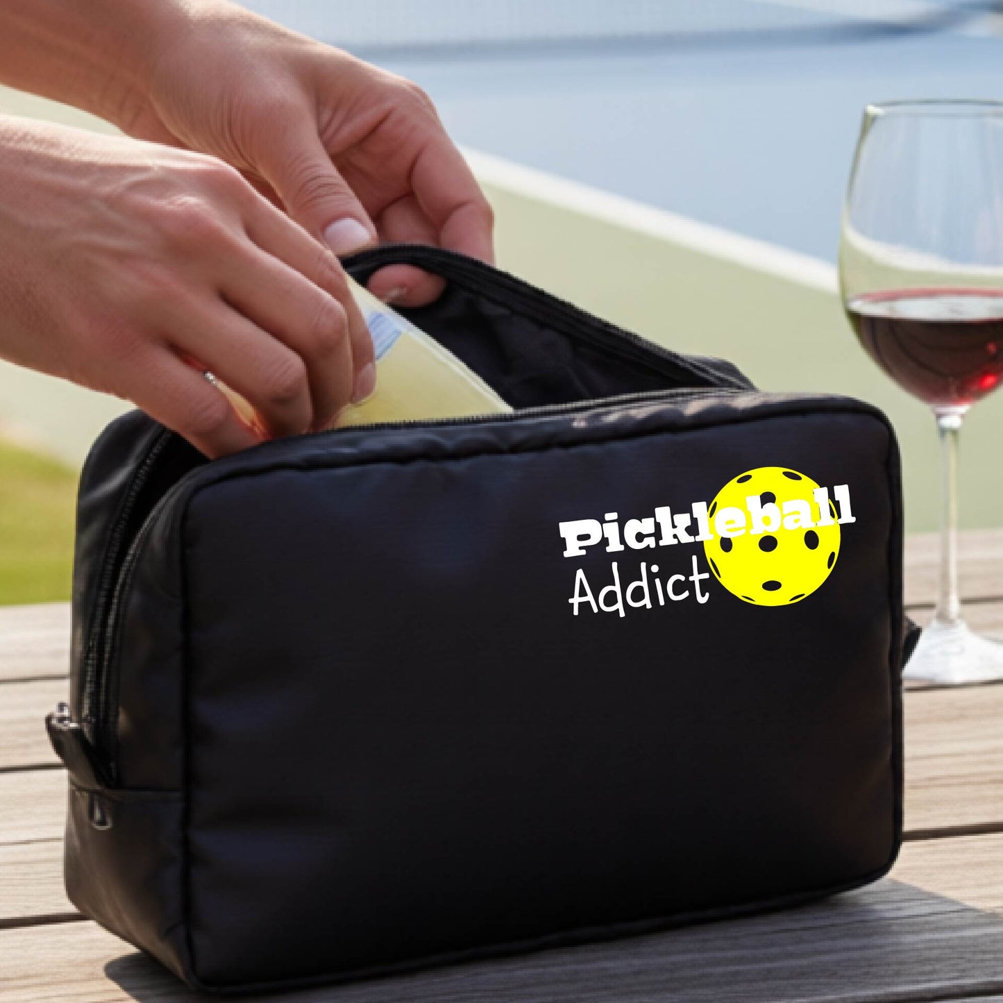 A black zippered cosmetic pouch with a printed white 'Pickleball Addict' logo with a yellow pickleball graphic.