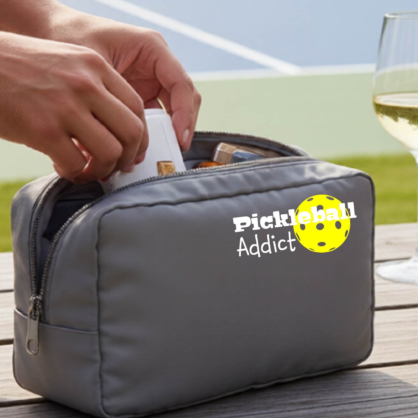 A gray zippered cosmetic pouch with a printed white 'Pickleball Addict' logo with a yellow pickleball graphic.