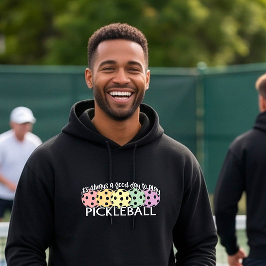 A man smiling outdoors wearing a black hoodie with a colorful pickleball graphic and the text 'it's always a good day to play PICKLEBALL' on the chest.