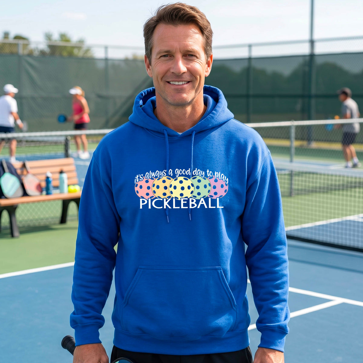 A man smiling outdoors wearing a royal blue hoodie with a colorful pickleball graphic and the text 'it's always a good day to play PICKLEBALL' on the chest.