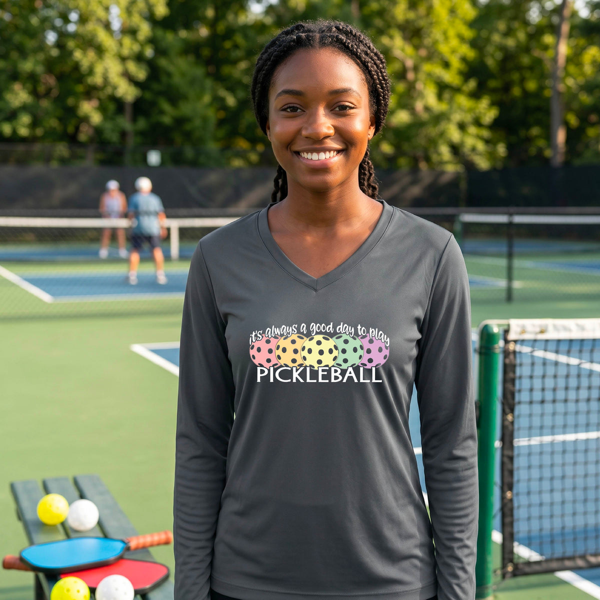 A woman laughing on a pickleball court wearing a gray long-sleeve V-neck shirt with a colorful pickleball graphic and the text 'it's always a good day to play PICKLEBALL'.